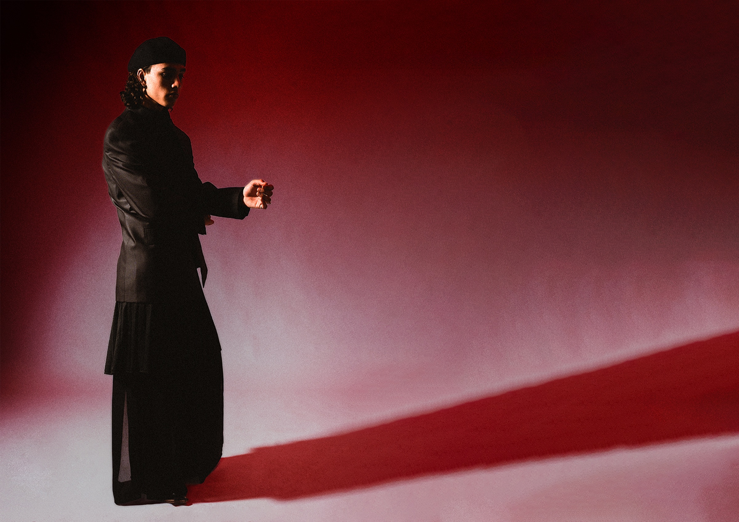 Model in dark layered tailoring against a red-lit backdrop