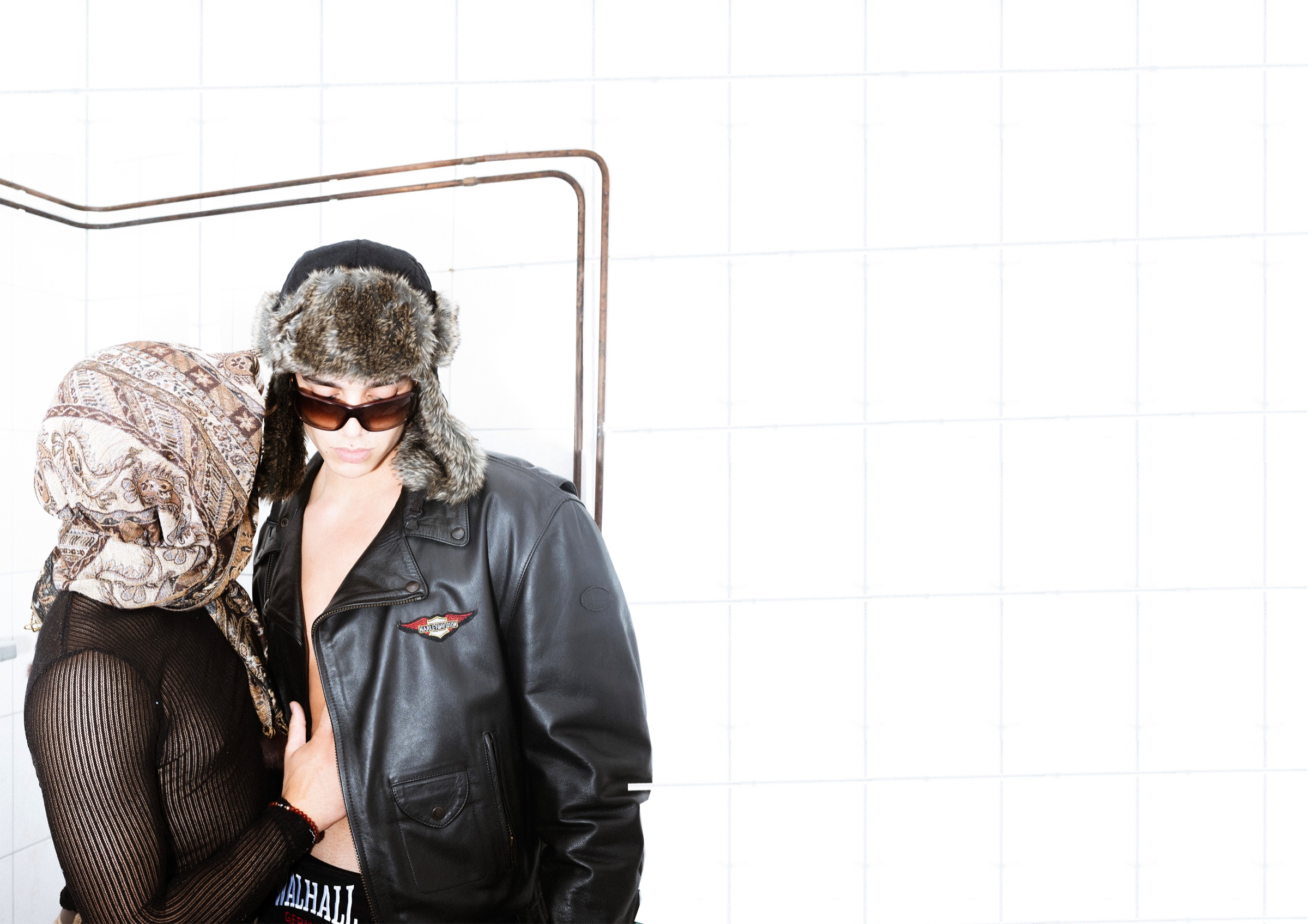 Two figures in layered vintage styling against white bathroom tiles