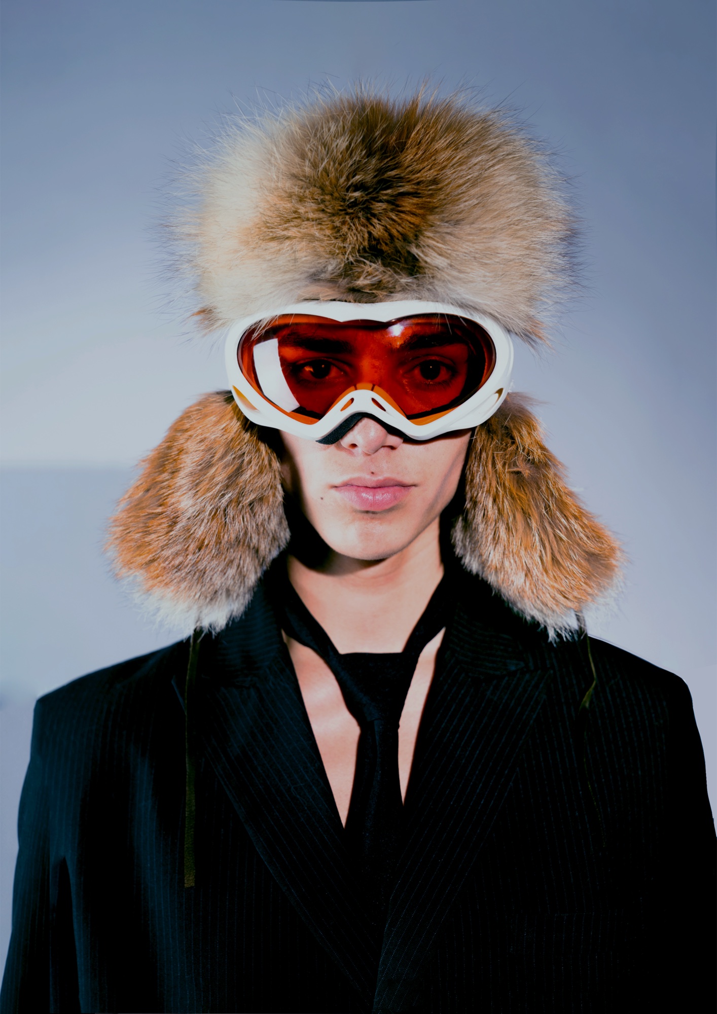 Front portrait in black tailoring, fur headwear and orange goggles